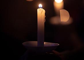 A candle lit against a dark background, with other candles out of focus, photo by Tim Umphreys