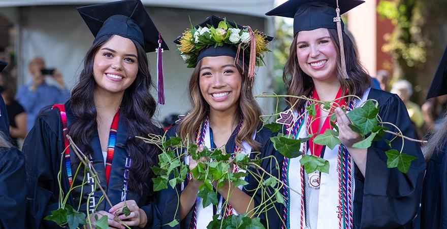 在SPU的常春藤剪枝仪式上，三位戴着帽子、身穿长袍的女学生自豪地举着她们的常春藤